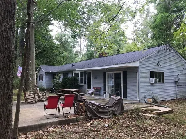A house with a patio and chairs in front of it surrounded by trees.