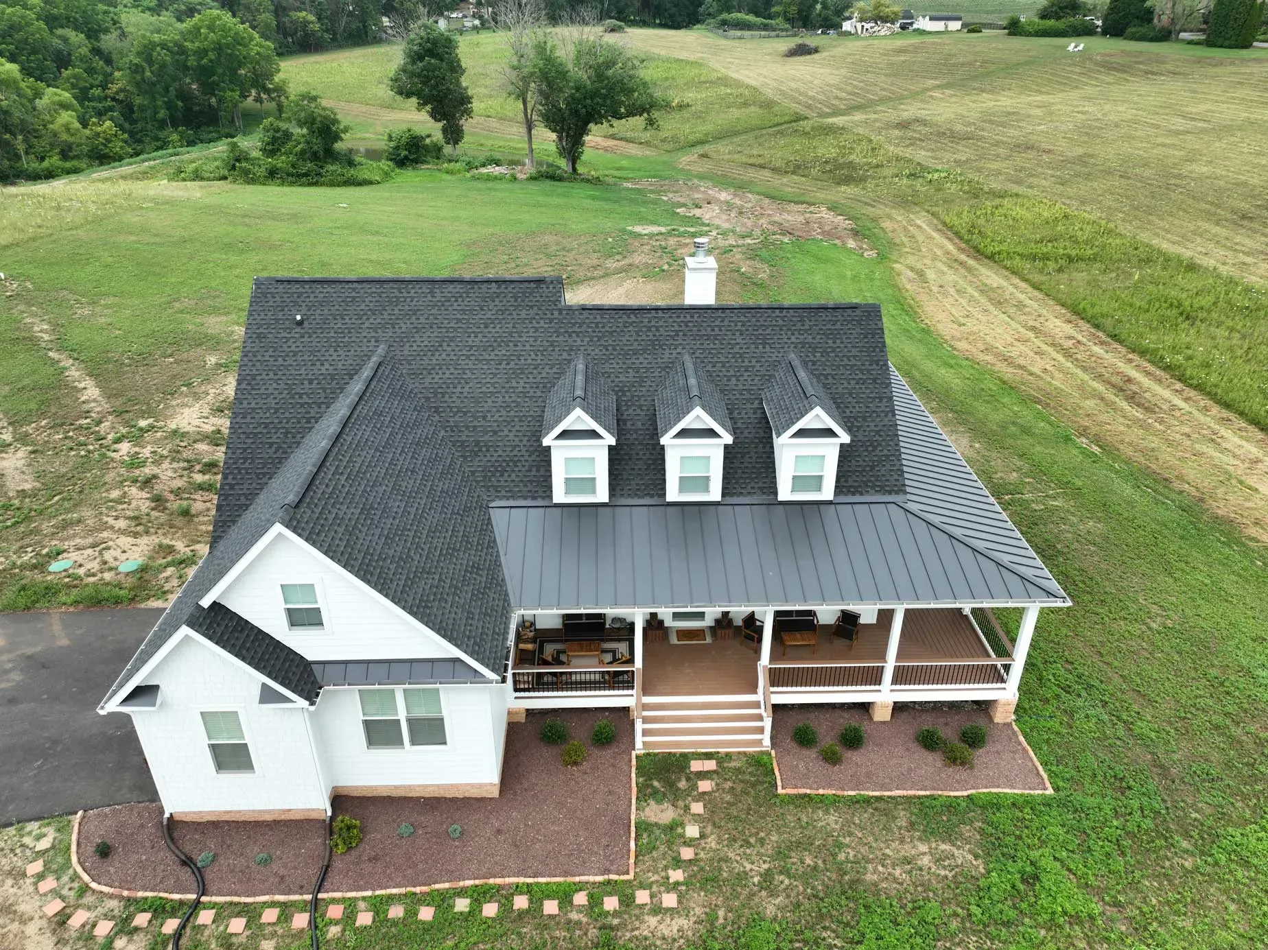 An aerial view of a white house with a black roof and a porch.