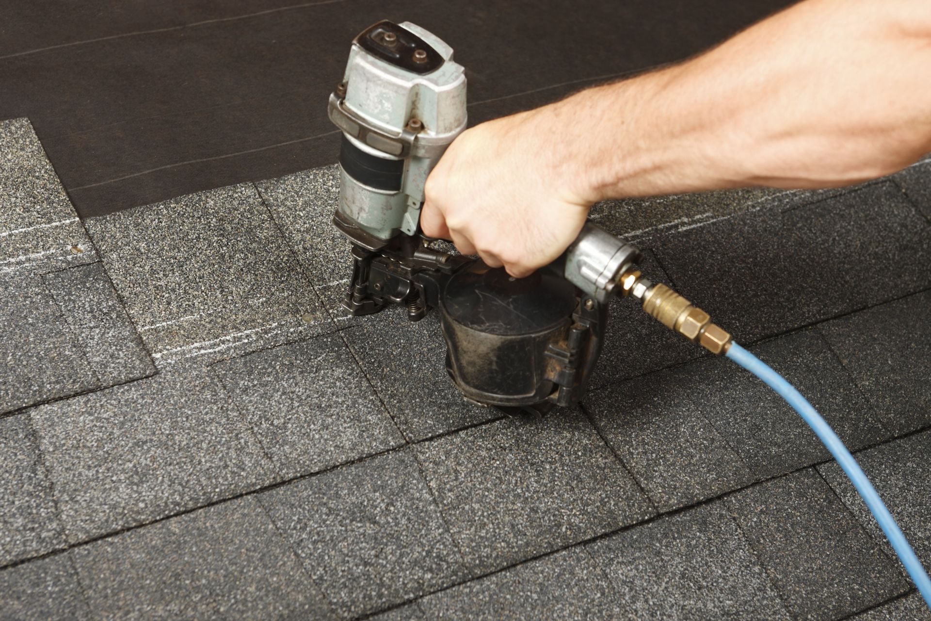 hand holding a nail gun while repairing the roof