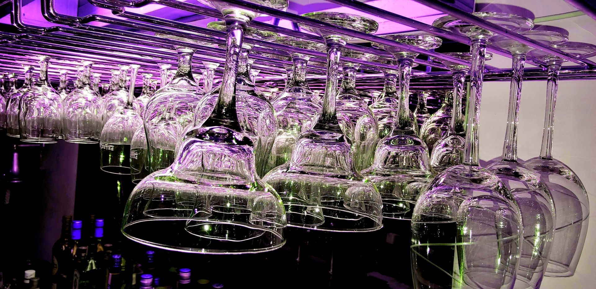 a bunch of wine glasses hanging from a rack in a bar .