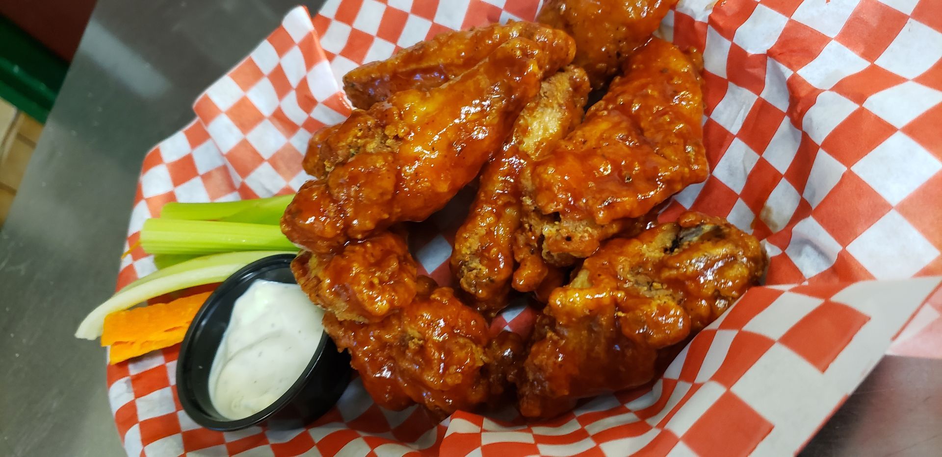 a basket of chicken wings with celery and ranch dressing on a checkered paper .