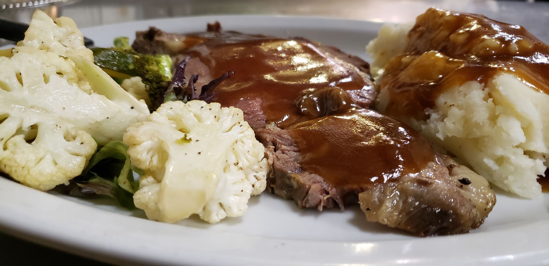 a white plate topped with meat , mashed potatoes and vegetables .