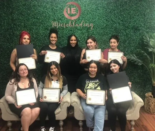 A group of women holding certificates in front of a wall that says microblading