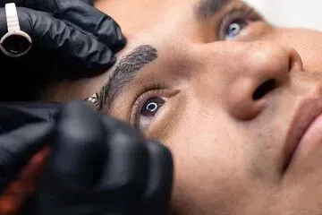 A man is getting a tattoo on his eyebrows.