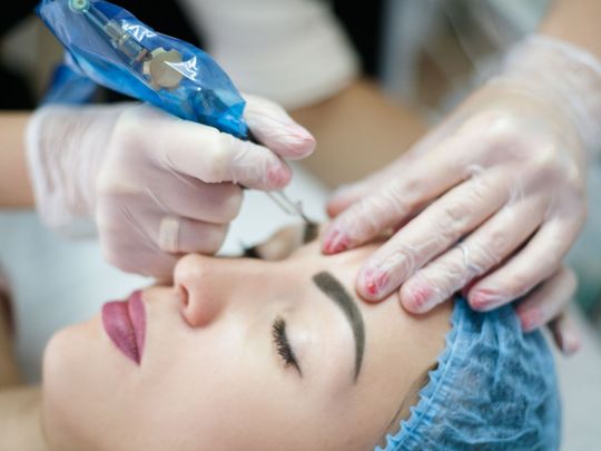 A woman is getting a permanent makeup tattoo on her eyebrows.