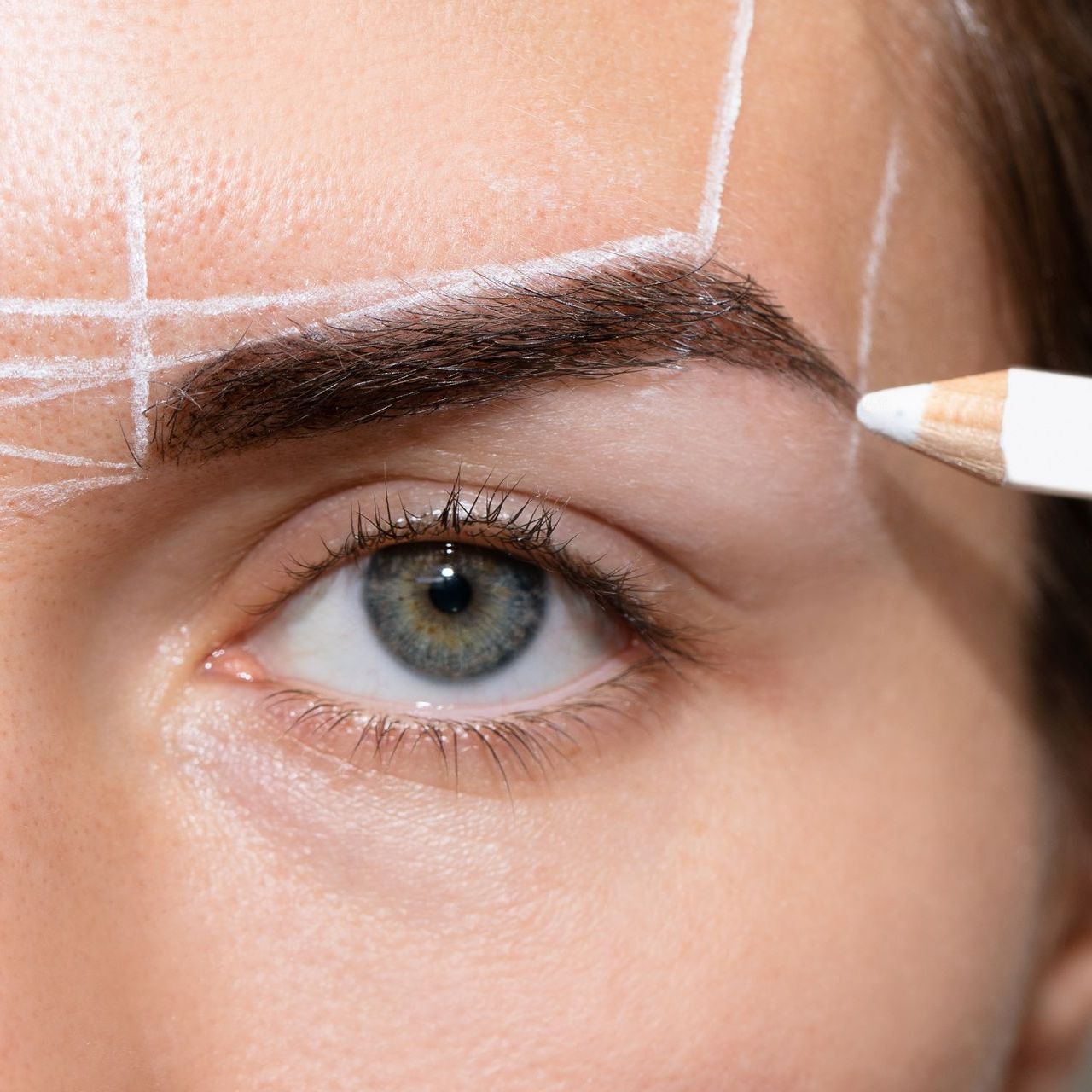 A woman is getting her eyebrows drawn with a pencil.