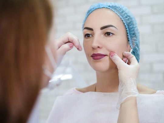 A woman is looking at her face in a mirror while a doctor examines it.