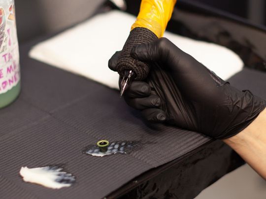 A person wearing black gloves is holding a yellow tattoo machine.