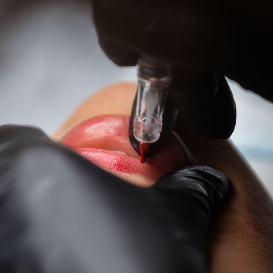 A woman is getting a permanent makeup tattoo on her lips.