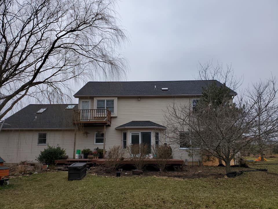 A large white house with a black roof is sitting in the middle of a grassy field.
