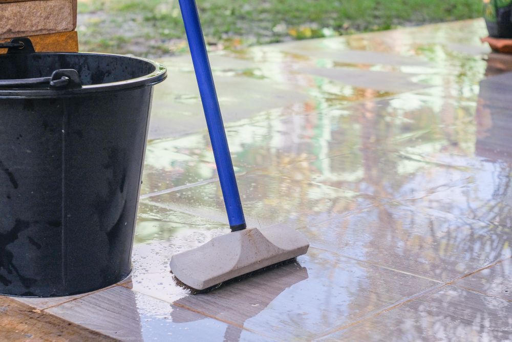 Blue mop and black bucket on a wet, tiled floor.