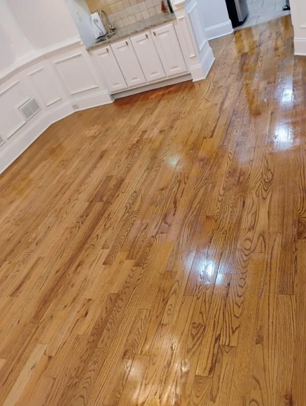 Wooden hardwood floors in a room, reflecting light. White cabinets and molding are visible.