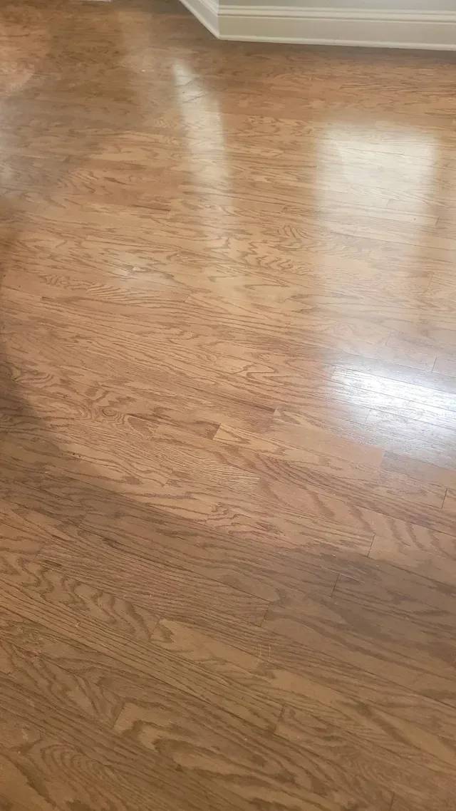 Close-up of a polished hardwood floor, with light reflecting off its surface, in shades of brown.