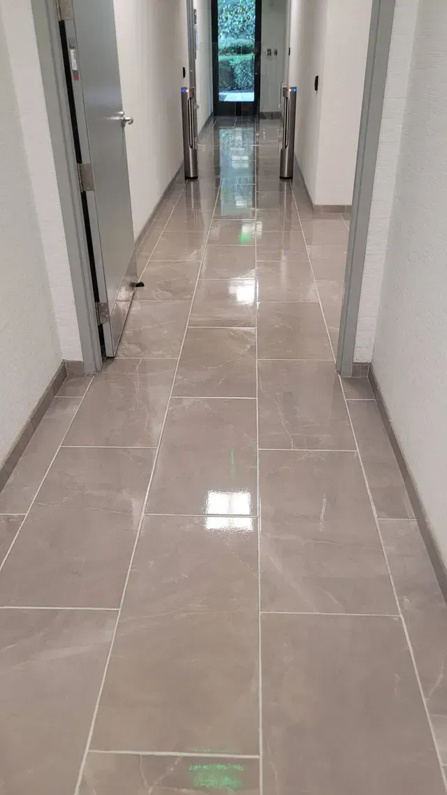 Long, tile-floored hallway with gray walls and doors, leading to a glass door at the end.