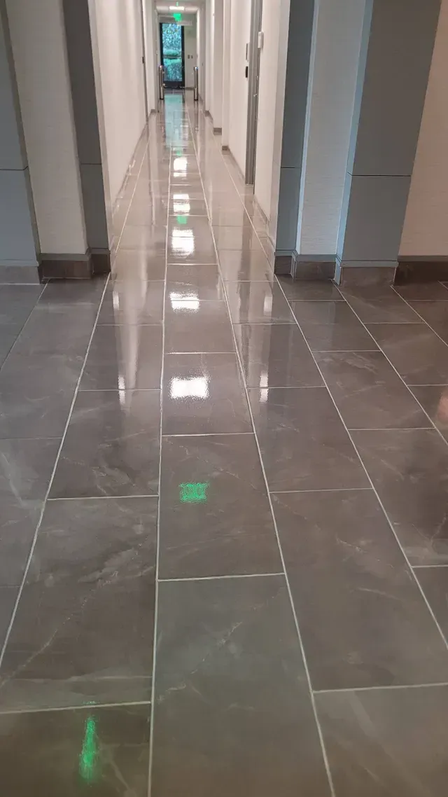 Long, shiny hallway with gray tiled floor, light reflecting from ceiling lights.