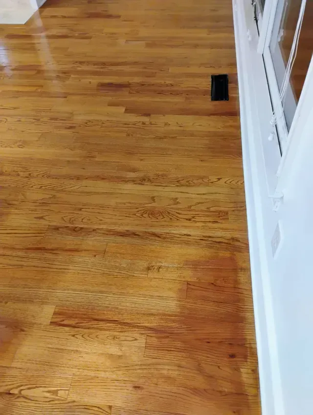 Shiny wooden floor with a black vent near a white wall.