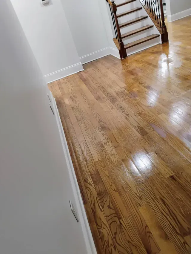 Hardwood floor hallway with stairs, white walls, and a glossy finish.