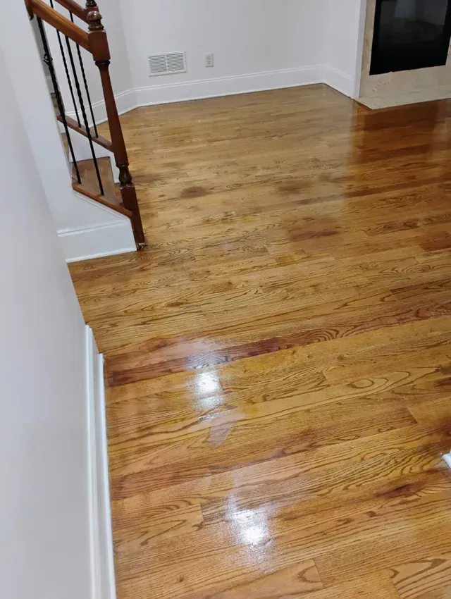Wood floor with a glossy finish in a room with white walls and a dark staircase.
