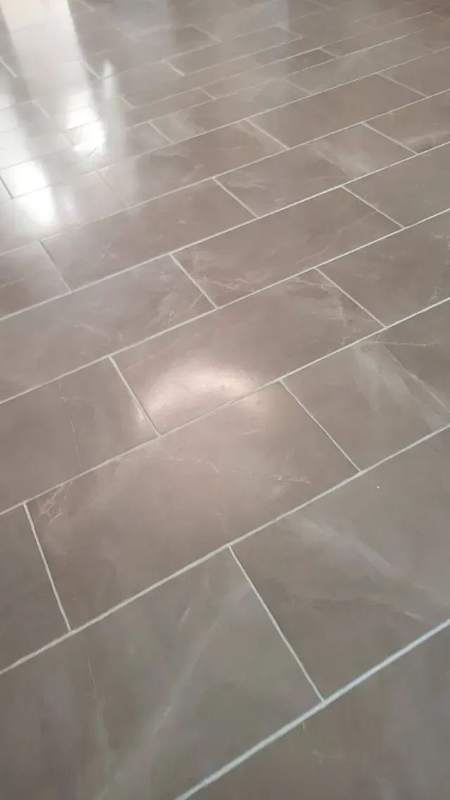 Gray rectangular tiles on a floor with white grout. The surface has a reflective, glossy appearance.
