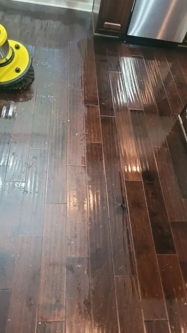 Yellow floor scrubber cleaning a dark wood floor, leaving streaks of water.