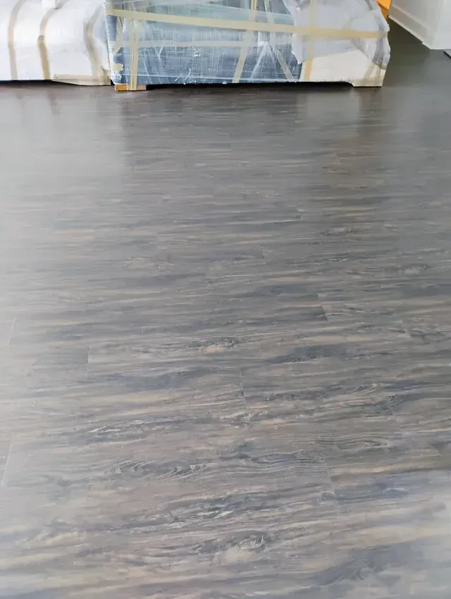 Dark wood-look flooring in a room, with a wrapped object in the background.