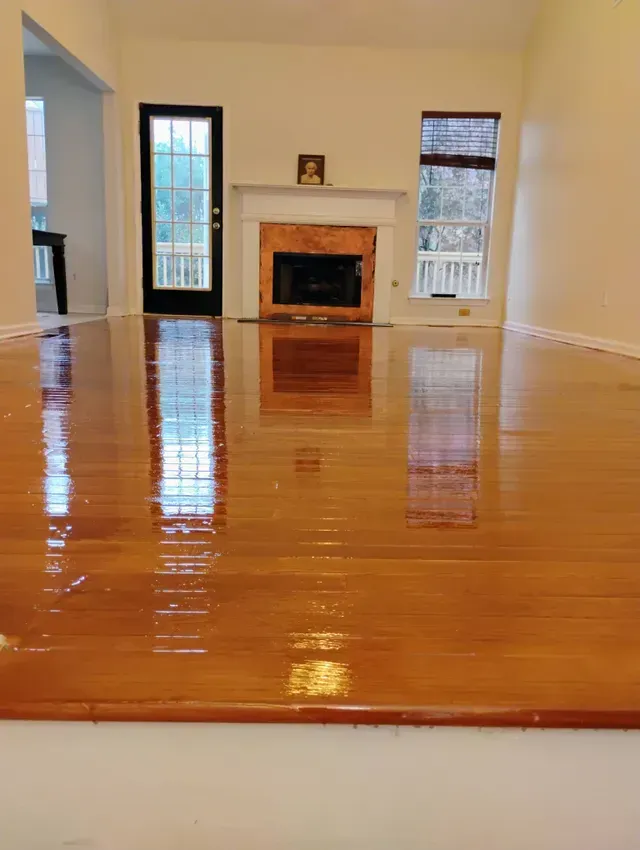 Shiny wooden floor reflecting a room's interior: fireplace, windows, and a dark door.