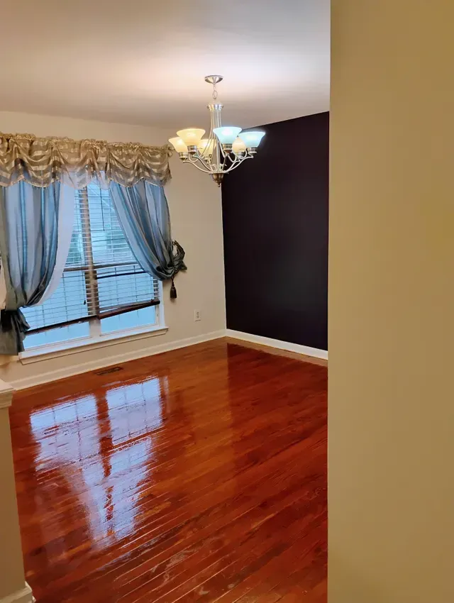 Dining room with shiny wood floors, dark accent wall, chandelier, and window with drapes.