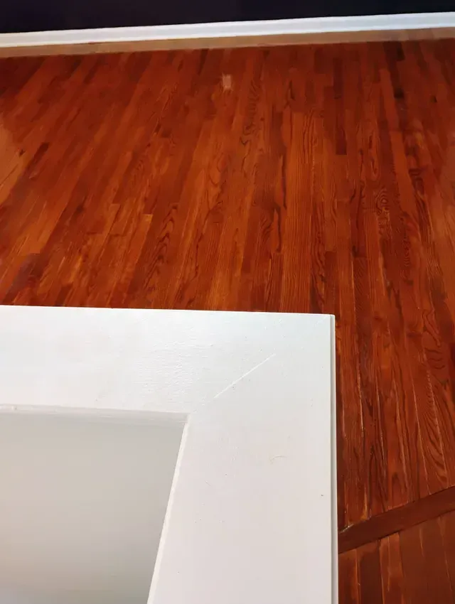 White door frame corner against a hardwood floor. Brown wood contrasts the white.