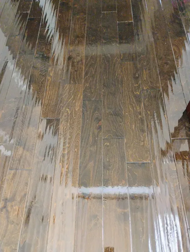 Wet, wooden-look flooring reflecting the ceiling. Brown and gray tones with water streaks visible.