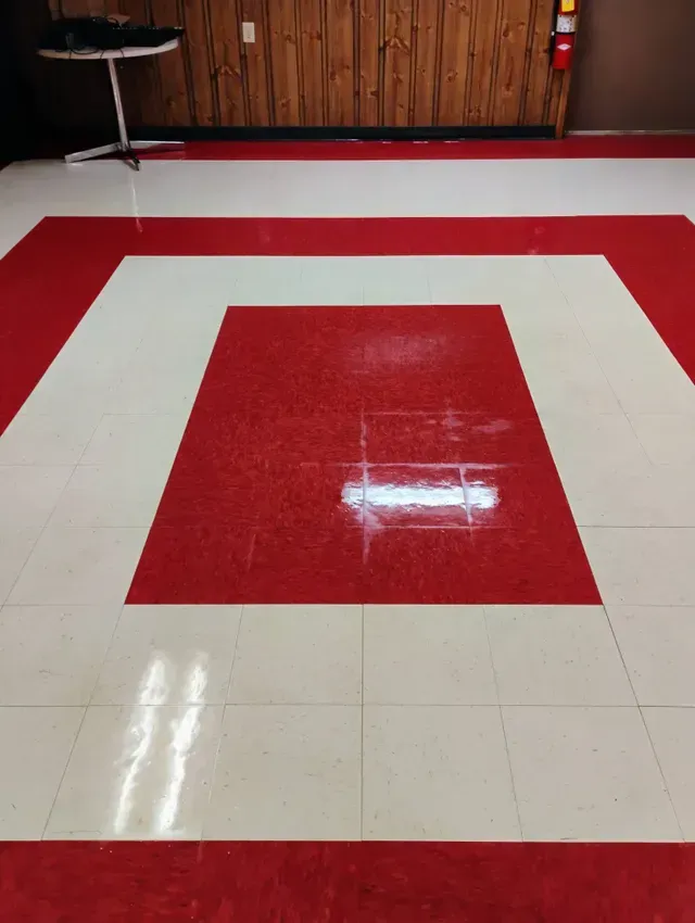 Red and white tiled floor in a room, with a small table and wood-paneled wall in the background.