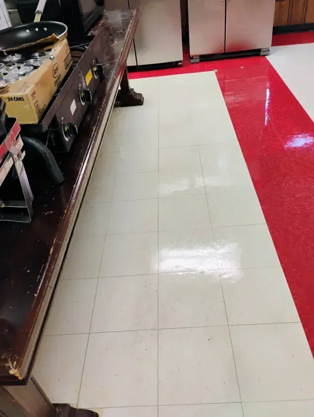 Long wooden counter with cooking appliances on beige and red tiled floor.