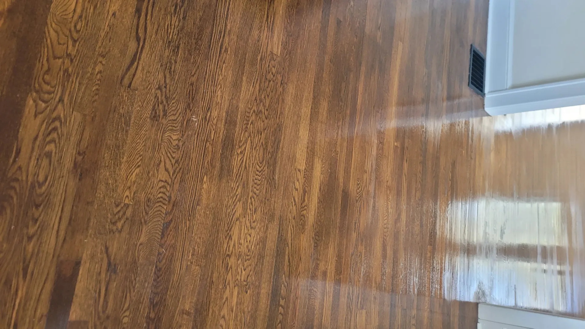 Wooden floor, wet with a streak of cleaner, next to a white cabinet.