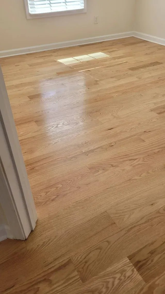 Light oak hardwood floor in a room, with a window providing sunlight across the planks.