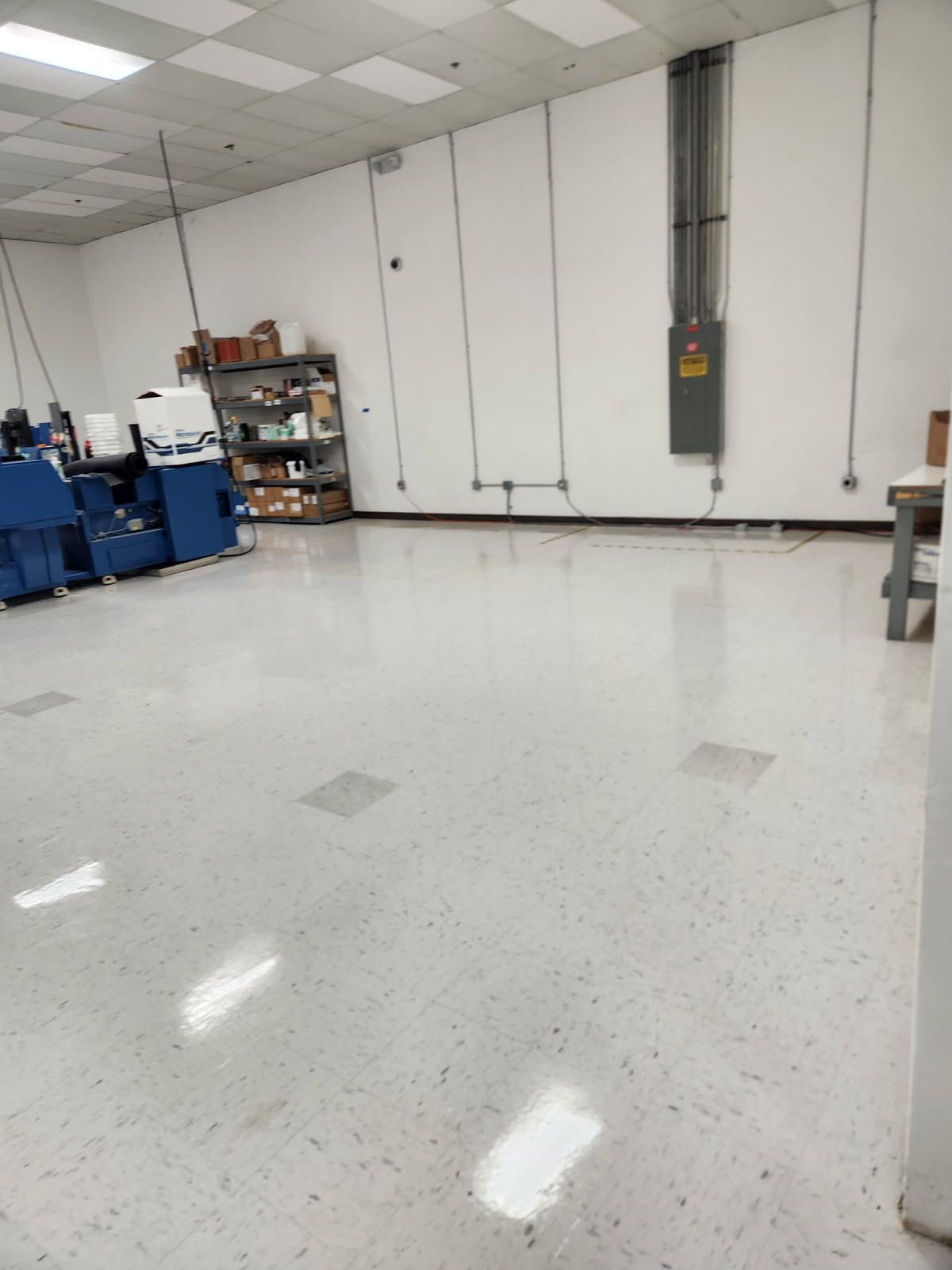 Empty, clean white room with electrical wiring, equipment on the left, and a shelf with supplies.
