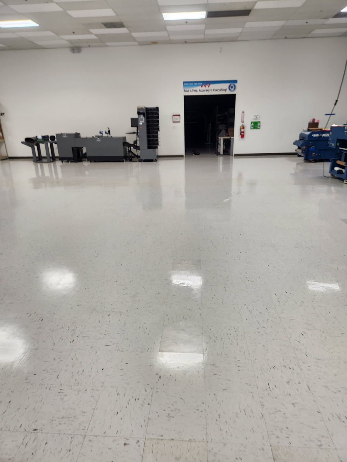 Empty, well-lit industrial space with machinery near walls, a large doorway, and a polished floor.