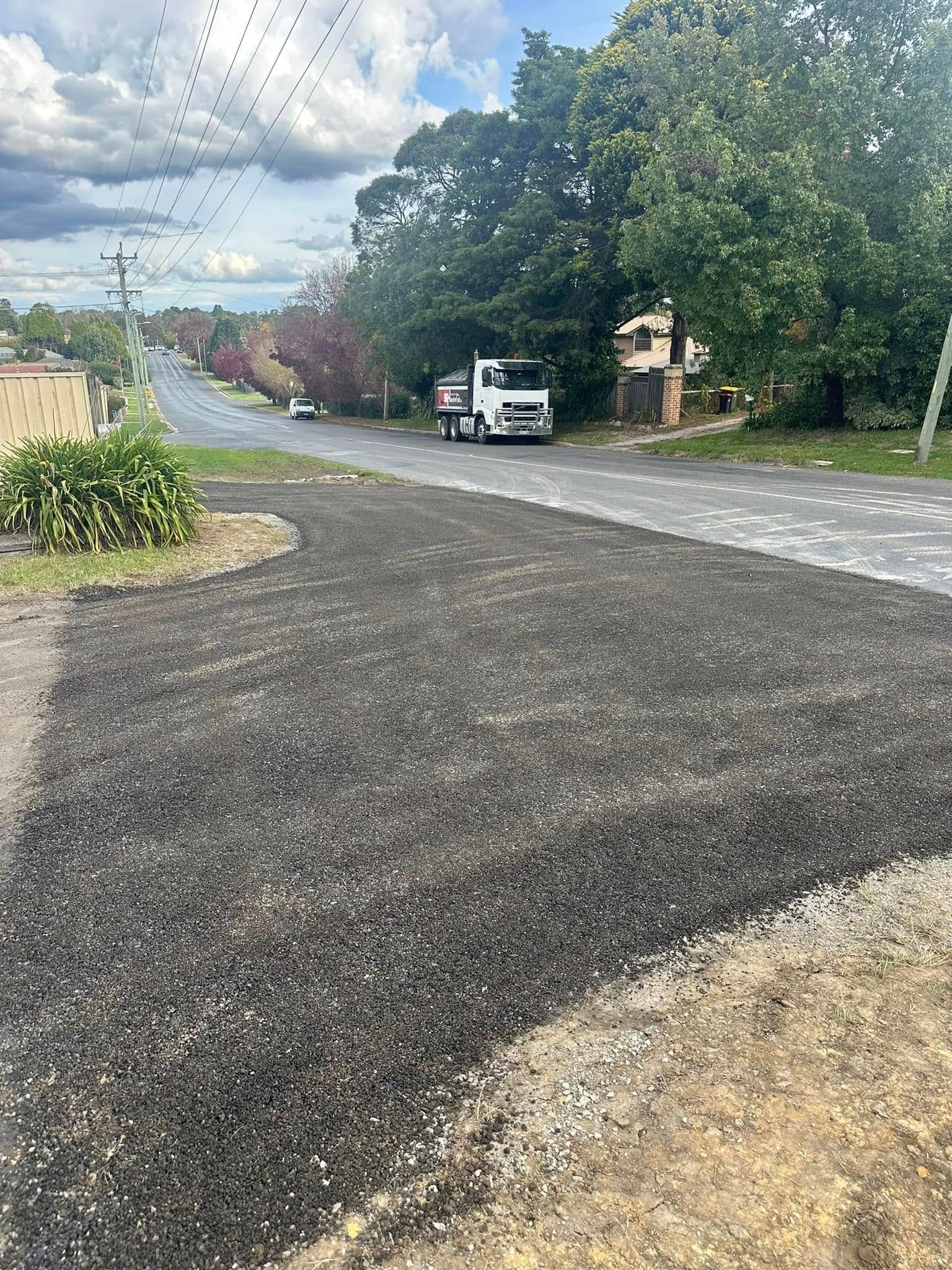 Quiet suburban street after rain with a white van parked under leafy trees and cloudy skies.