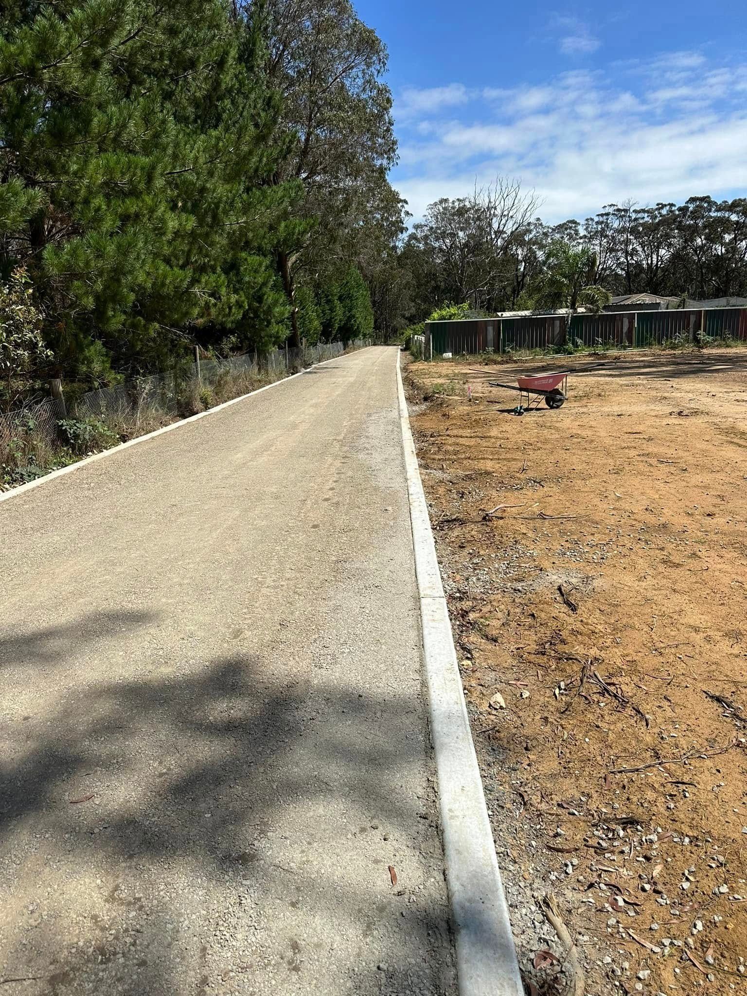 Gravel path beside a dirt field, lined with trees and a white edge marking.