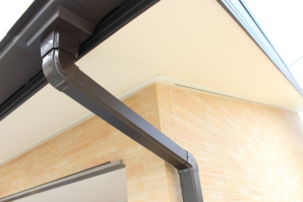 Close-up of a dark brown gutter and downspout on a house roof corner.