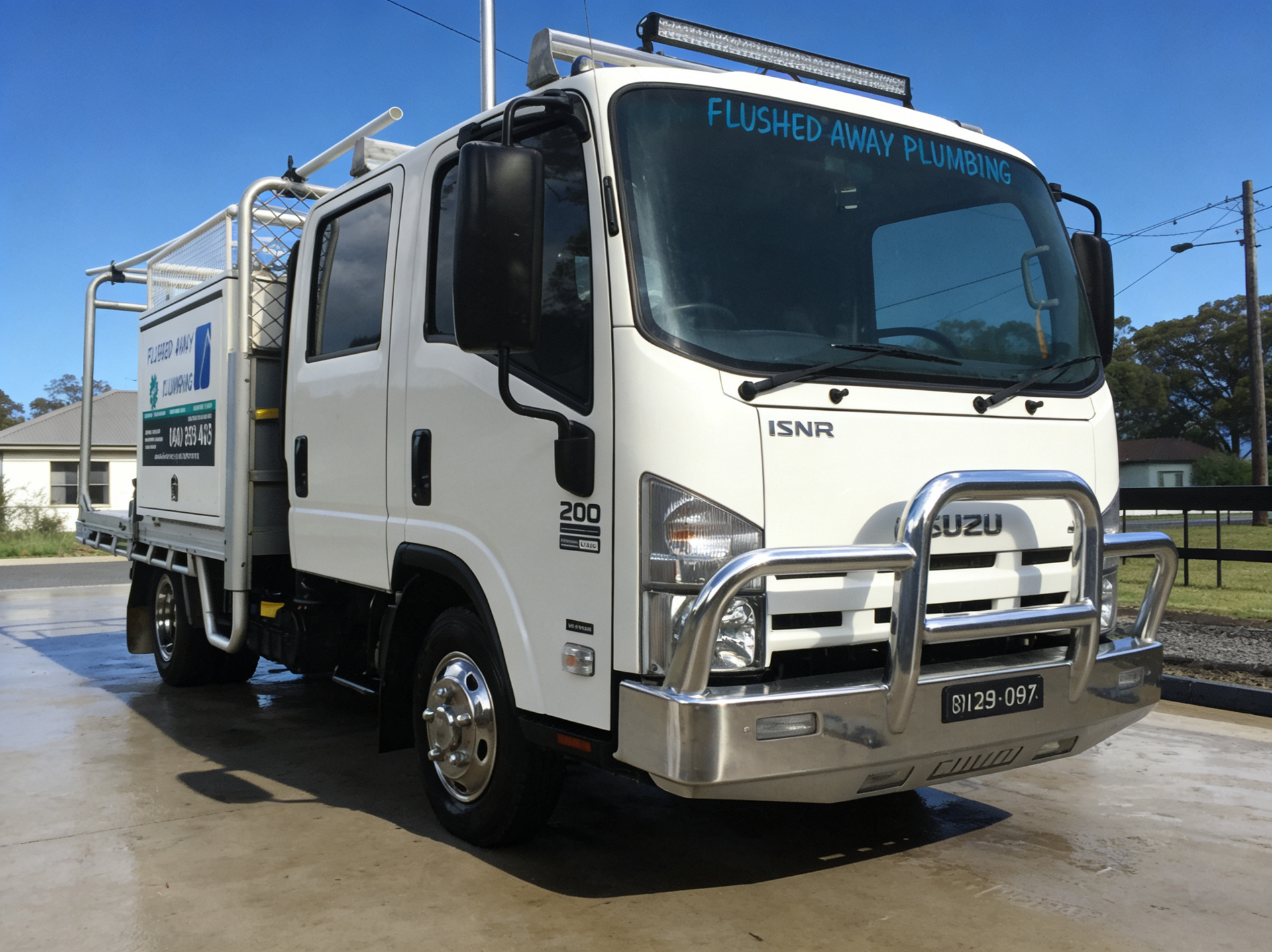 White Isuzu flatbed truck with chrome bull bar parked outdoors on a sunny day