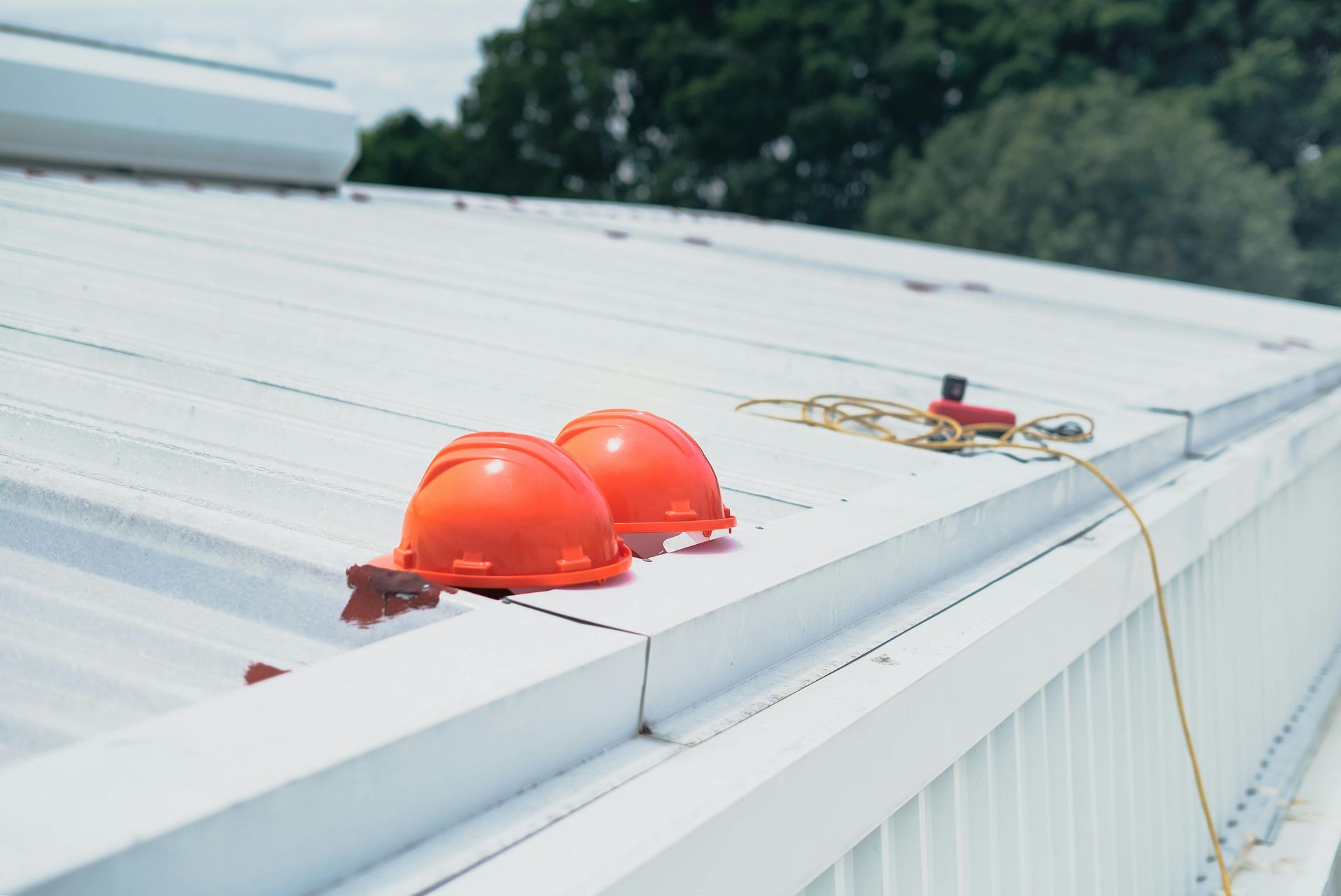 Two orange hard hats on a white rooftop near safety gear and a cord