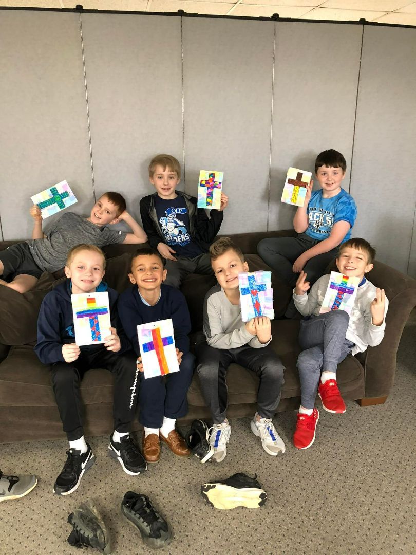 A group of young boys are sitting on a couch holding crosses