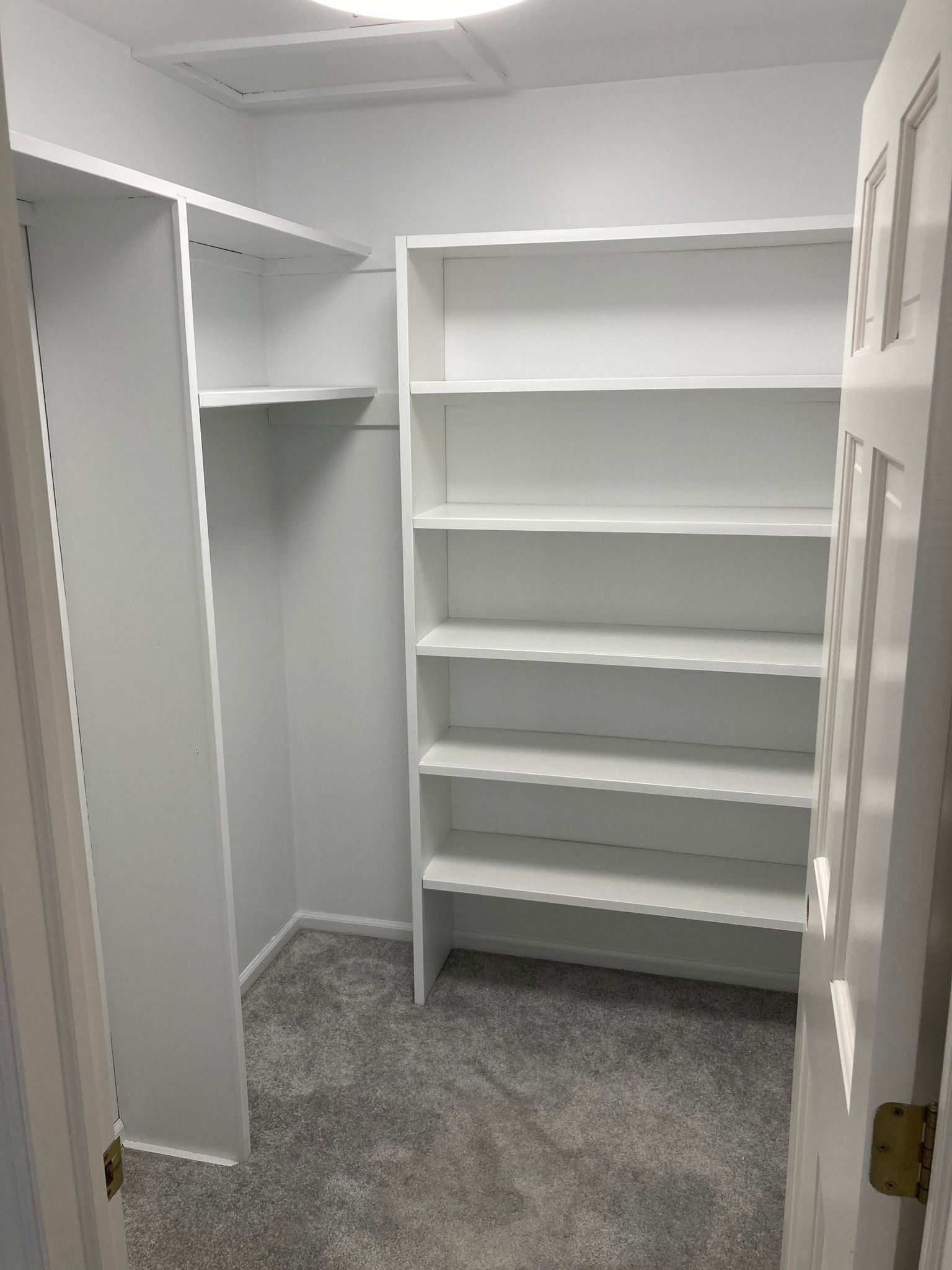 Empty, white closet with built-in shelves and a hanging rod, carpeted floor.