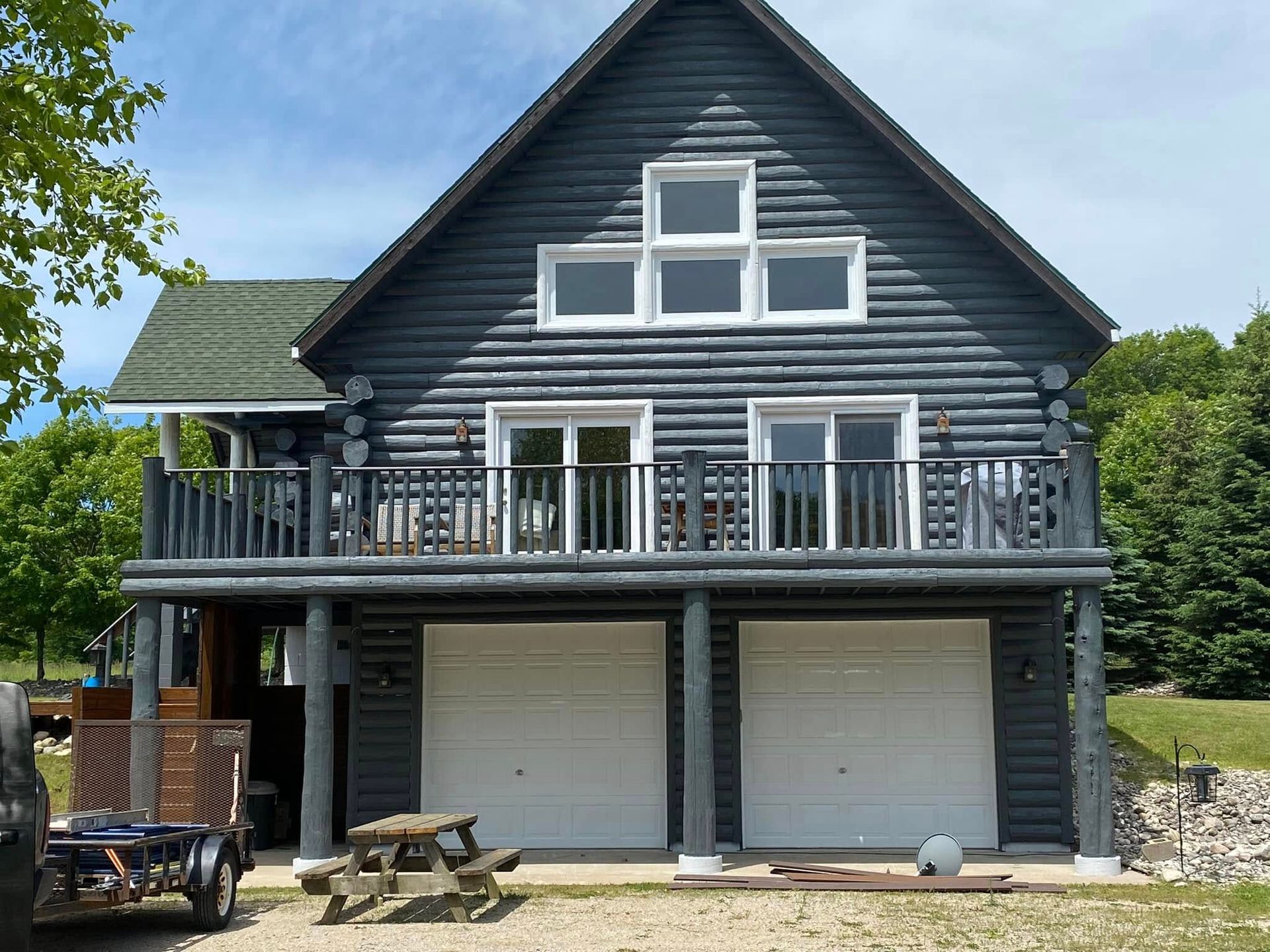Log cabin with two garage doors and balcony painted dark blue.