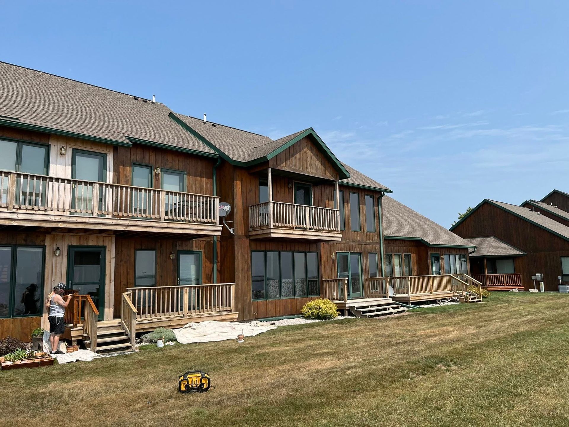 Brown wood houses with balconies on a grassy hillside under a clear blue sky.