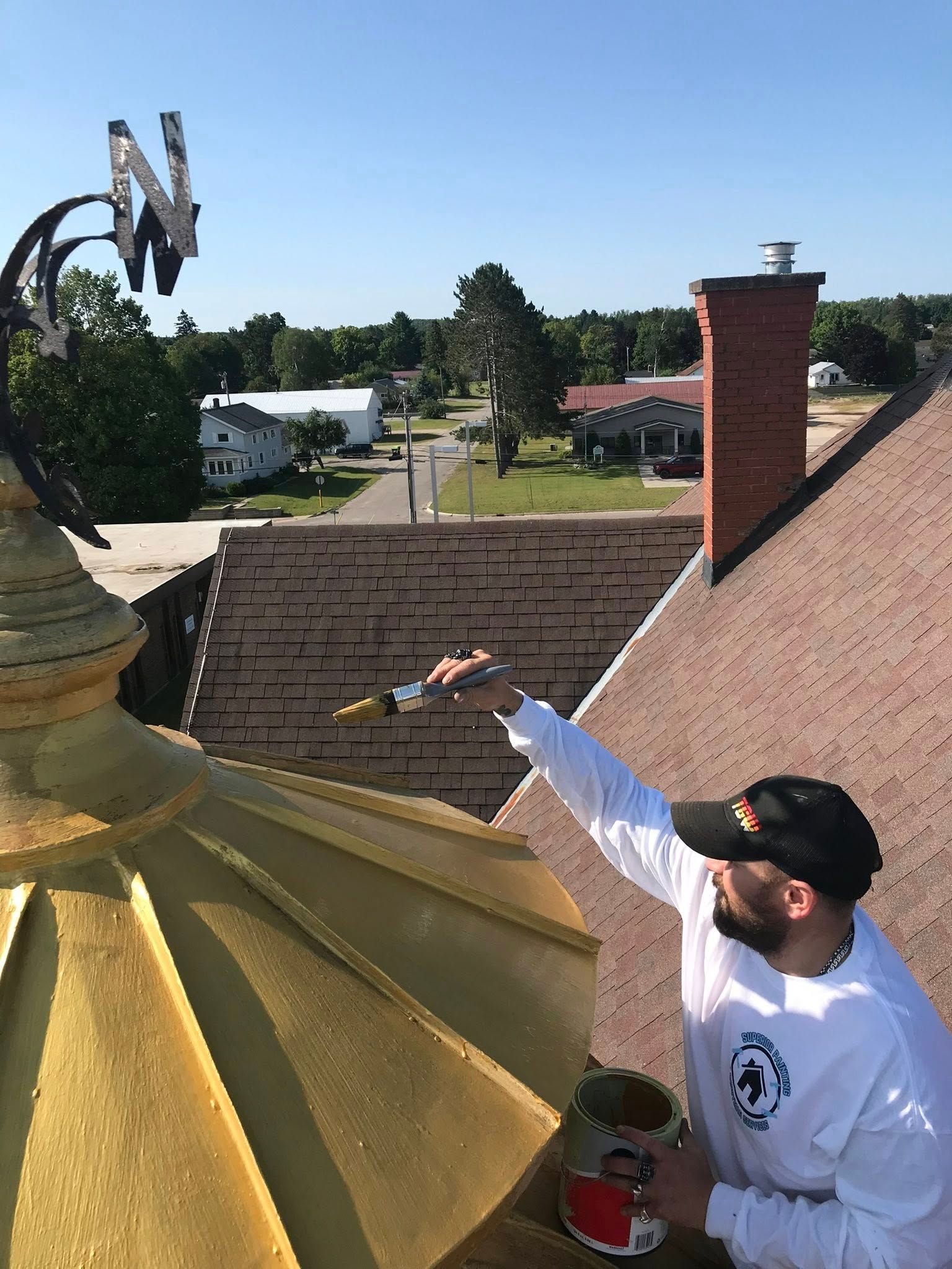 Person on roof painting a gold dome. A paintbrush is in hand, town in background.