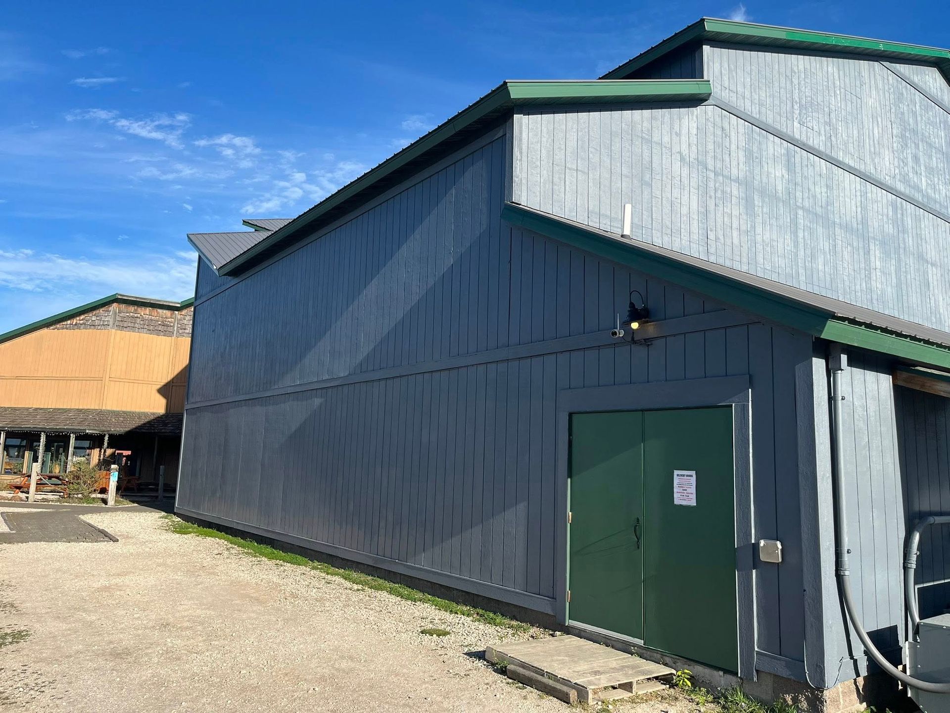 Gray barn-like building with green trim and doors on a sunny day.