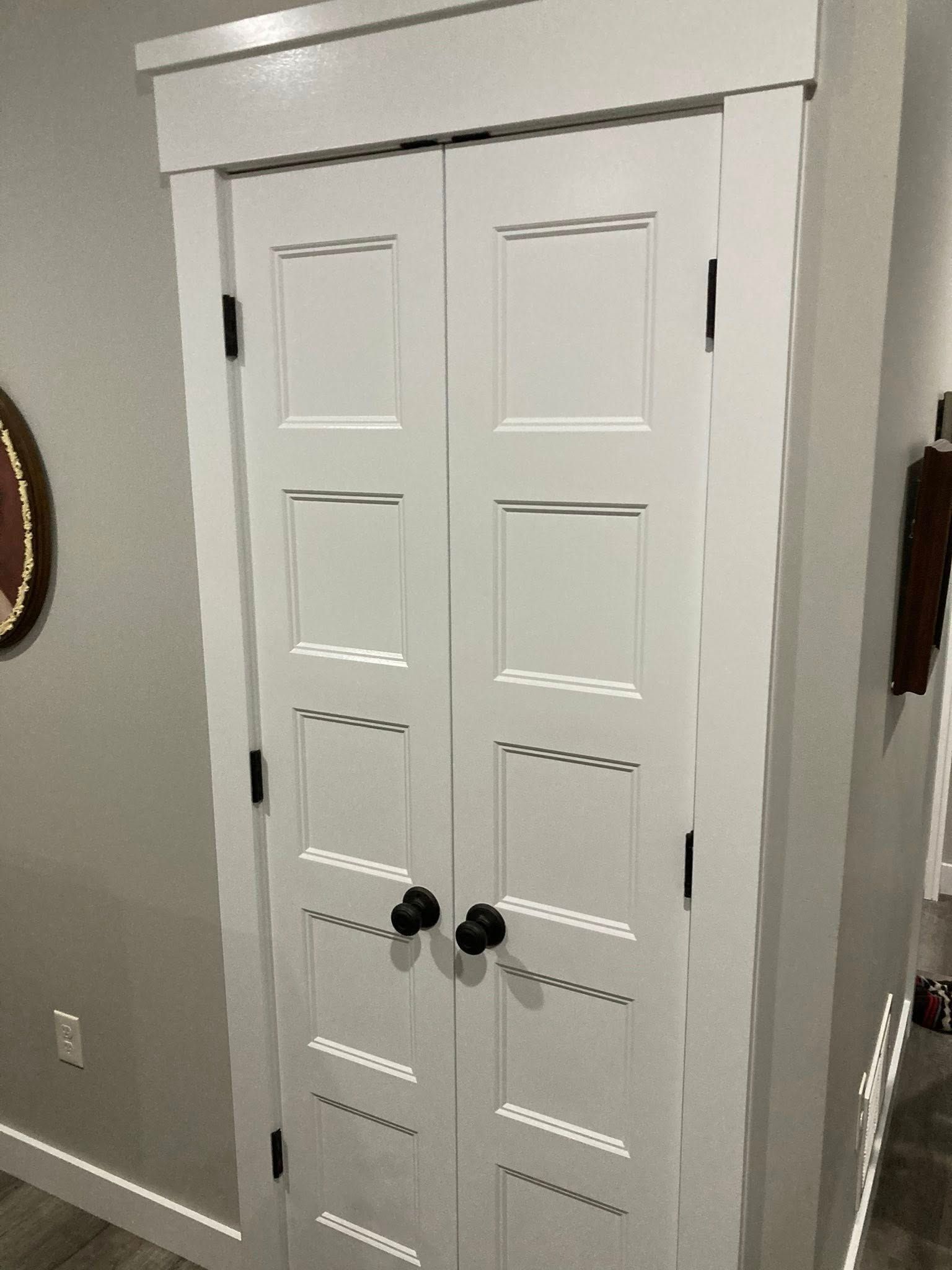 White double doors with black hardware, framed in white, in a room with light gray walls.