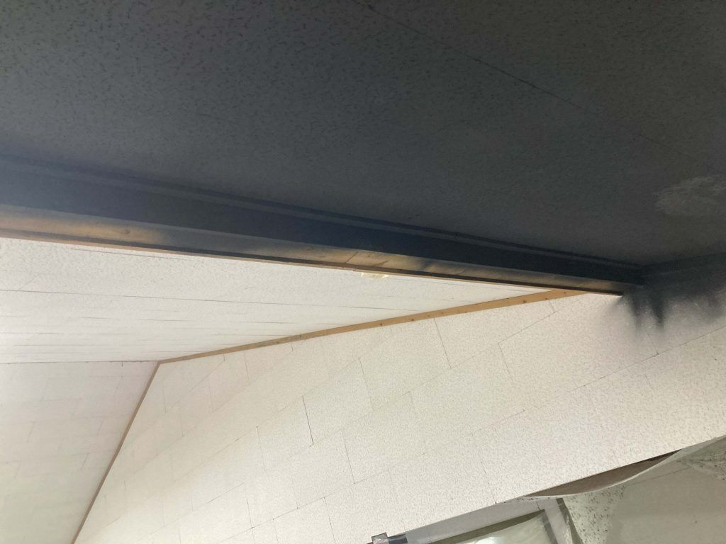Blackened ceiling near a wall, likely from a fire. The wall is off-white and angled.