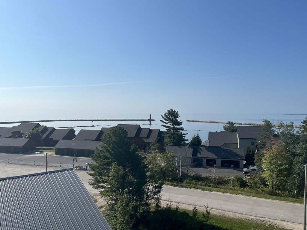 View of a lake with a pier, houses, and trees under a clear blue sky.