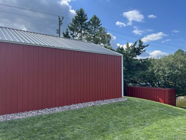 Red metal-sided building with silver roof, green lawn, gravel border, blue sky with clouds.